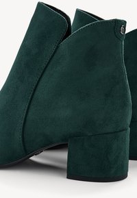 Zelené semišové kotníkové boty s krátkým blokovým podpatkem, nabízející rozdělený design na kotníku a černý knoflíkový akcent.