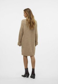 Abito in maglia beige con maniche lunghe, polsini a coste e taglio medio, abbinato a stivaletti neri con tacco.