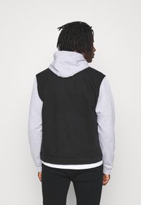 Czarna kurtka dżinsowa z szarą bluzą z kapturem pod spodem. Charakteryzuje się luźnym krojem i czystymi liniami, prezentując warstwowy design.