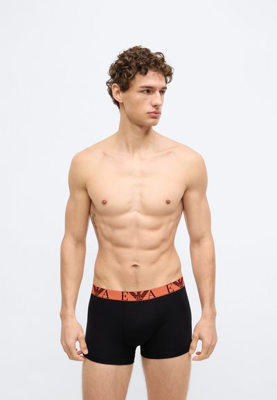 Boxer aderenti in cotone nero con una fascia in vita arancione caratterizzata da un motivo logo ripetuto. Progettati per una silhouette aderente, con una texture liscia.