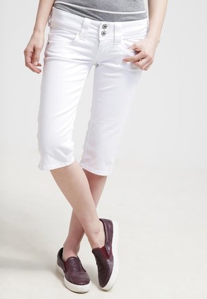 Witte cropped broek met een gladde textuur, voorzien van een knoopsluiting en voorzakken. Gecombineerd met donker bordeauxkleurige instappers.