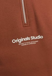 Ruskea huppari, jossa on puolivetoketjukaulus, pehmeä tekstuuri ja valkoisella painettuna teksti "Originals Studio" logotiedoilla.
