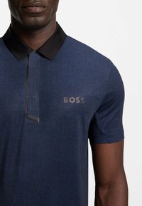 Dunkelblaues Poloshirt mit strukturiertem Stoff, schwarzem Kragen und eingeprägtem "BOSS"-Logo auf der linken Seite. Kurzärmlig und mit elegantem Design.