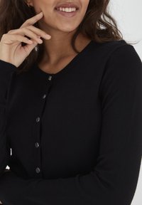 Cardigan nero realizzato in tessuto morbido, caratterizzato da un scollo rotondo e chiusura con bottoni con accenti metallici lungo la parte anteriore.