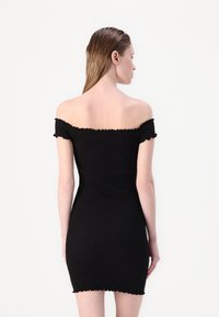 Robe mini noire à épaules dénudées en tissu texturé, ornée de volants aux manches et à l'ourlet, avec une silhouette ajustée.