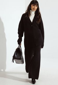 Črn oversized pleteni cardigan, visok vrat beli top, široke črne hlače, črne čevlje s peto in strukturirana črna torba.