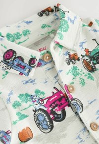 Chemise à boutons pour enfants en tissu blanc, ornée d'imprimés de tracteurs colorés, d'arbres verts, de boutons marron et d'une finition texturée.