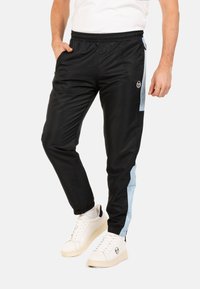 Pantalons de survêtement noirs avec une taille et des poignets élastiques, présentant des panneaux latéraux bleu clair. Associés à des baskets blanches.