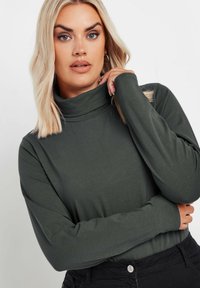 Oliwkowy golf wykonany z miękkiego materiału, z długim rękawem i luźnym krojem. Połączony z czarnymi spodniami, z minimalnymi akcentami wyposażenia.