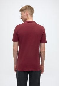 Burgundy polo shirt with short sleeves, classic collar, and a smooth texture. Back view shows shoulder seam and simple design.