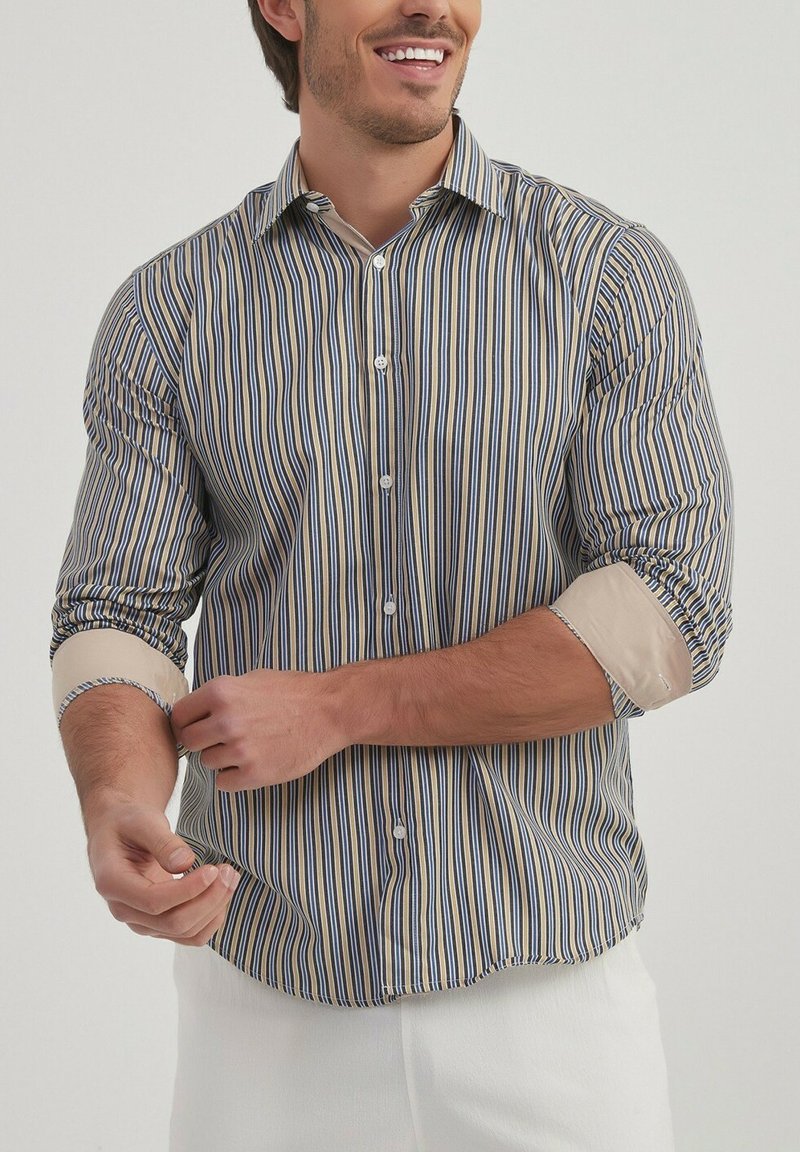 Chemise à manches longues avec des rayures verticales bleu, jaune et blanc. Présente un devant à boutons et des poignets beige retroussés. Tissu léger.