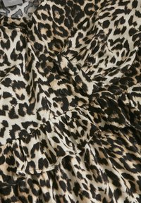 Blus i leopardmönster i lätt tyg, med svarta knappar, volangdetaljer längs framsidan och en blandning av bruna och svarta mönster.