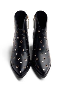 Bottines en cuir noir avec un bout pointu, ornées de détails en œillets dorés et de zips latéraux, présentant une texture lisse.