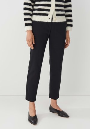 Pantalons slim noirs au toucher lisse, longueur cheville, associés à des ballerines noires à bout pointu et à un cardigan en tricot à rayures.