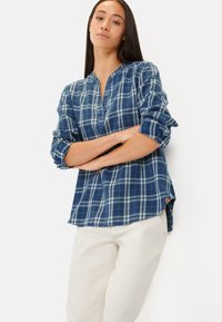 Blau kariertes Hemd mit Henley-Ausschnitt, aufgerollten Ärmeln und abgerundetem Saum. Hergestellt aus weichem Stoff mit hellblauen und dunkelblauen Karos.