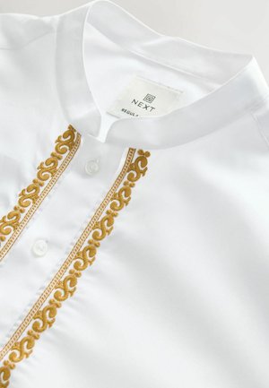 Cămașă albă cu guler în picioare și închidere cu nasturi, având broderie aurie ornate pe plăcuța frontală și țesătură texturată.