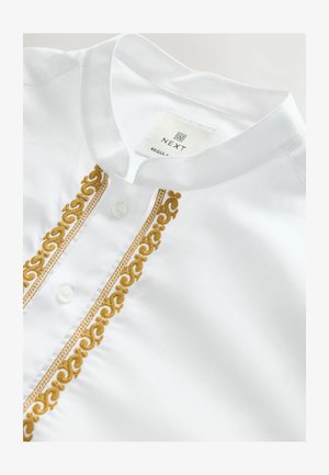 Chemise blanche à col montant et fermeture à boutons, ornée de broderies dorées sur le plastron et d'un tissu texturé.