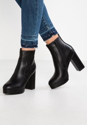 Schwarze Leder-Plateau-Stiefeletten mit klobigen Absätzen, getragen zu blauen Skinny-Jeans mit ausgefranstem Saum auf hellem Hintergrund.