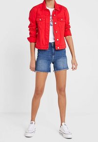 Röd jeansjacka med knappstängning framtill, kombinerad med ljusblå jeansshorts med fransiga kanter, och vita canvas-sneakers. Minimalistisk design.