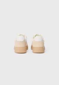 Hvite sneakers med beige semsket hælkappe og lys brun gummisåle. Har et minimalistisk design og glatte teksturer, merket "ARKK" på baksiden.