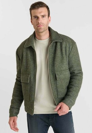 Groene, gestructureerde jas met een kraag en twee voorzakken, gecombineerd met een lichtgekleurde shirt. Slim fit, ritssluiting aan de voorkant.