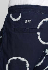 Námořnické modré šortky s bílými kruhovými vzory, s zadní kapsou a vyšitým logem nůžek. Vyrobené z lehké látky.
