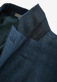 Dunkelblaues Wolljackett mit strukturiertem Stoff, einem glatten Innenfutter, einem strukturierten Kragen und sauberen Nähten.