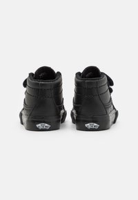 Een paar zwarte Vans high-top sneakers met klittenband, van achteren getoond, met de nadruk op het "Off The Wall" logo op de zolen.