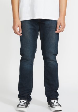 Donkerblauwe denim jeans met een slim fit, met een klassiek vijf-pocket ontwerp en contrasterende stiksels. Gecombineerd met zwarte sneakers.