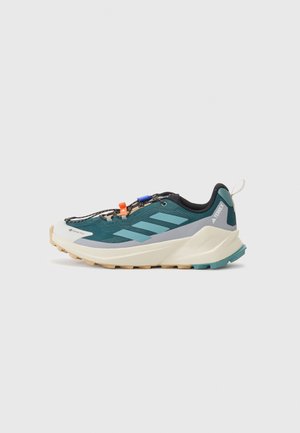 Sapata de trail running em verde escuro e preto, com um cabedal texturizado, riscas laterais proeminentes e uma sola robusta para uma melhor aderência.