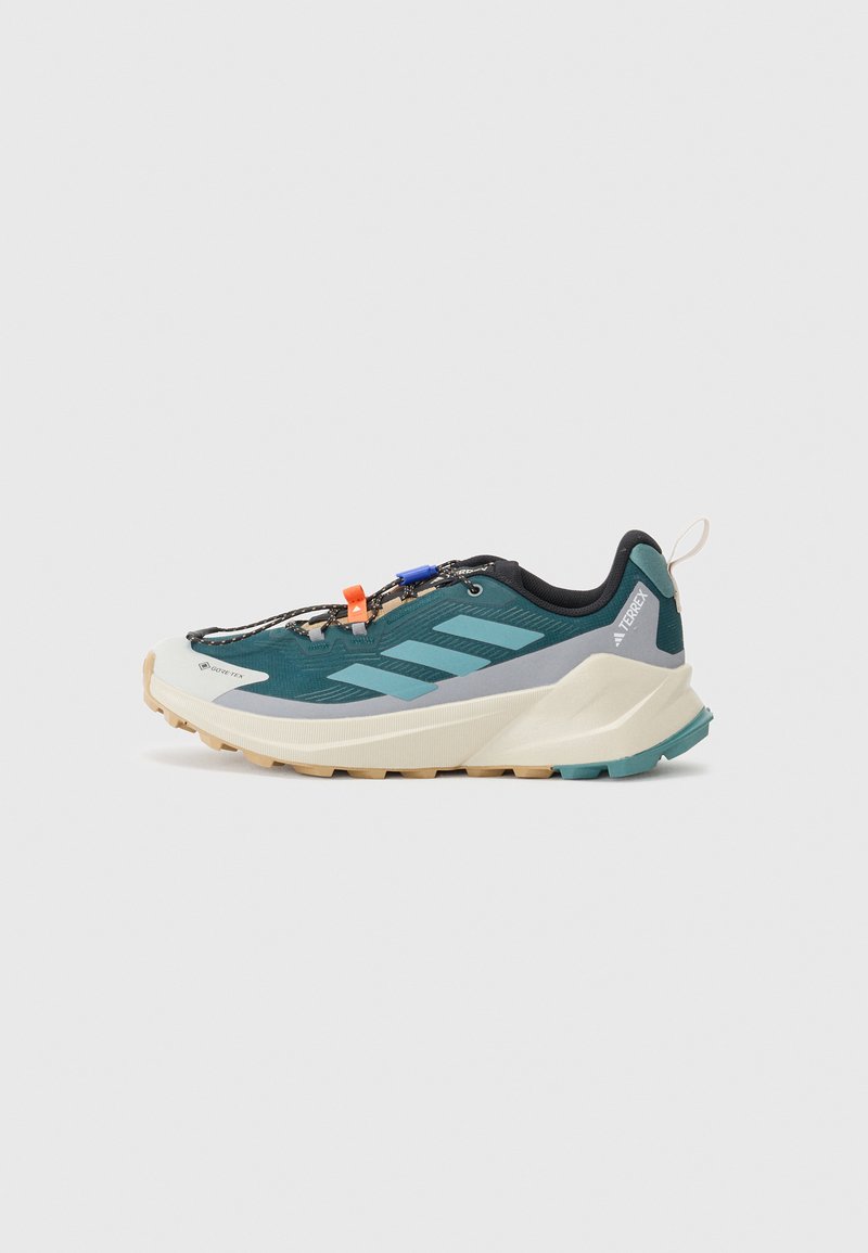 Trail running shoe in dark teal and black, featuring a textured upper, prominent side stripes, and a rugged sole for enhanced grip.