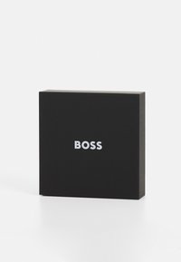 Scatola rettangolare nera con finitura opaca, con la parola "BOSS" in bianco, centrata sulla parte anteriore. Texture liscia, design minimal.