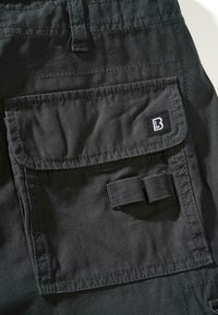 Črne hlače cargo iz tkanine z velikim žepom s poklopcem, kontrastnim šivom in majhno etiketo z logotipom "B". Teksturiran material in nastavljiv trak.
