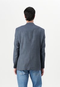 Blå rutad kavaj med en slits, notchade slag och två knappar. Texturerat tyg kompletterar denimjeans.