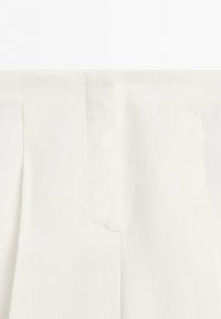 Gros plan sur un vêtement blanc sur mesure avec des coutures verticales et un détail central de tissu superposé.