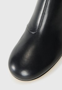 Fekete sima bőrből készült bokacsizma lekerekített orral és látható varrási részletekkel, fehér háttérrel.