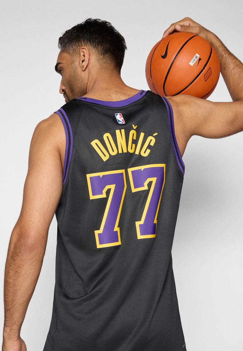 Camiseta de baloncesto negra con acentos en púrpura y amarillo. Muestra "DONČIĆ" y "77" en la parte posterior. Textura suave con un diseño deportivo.