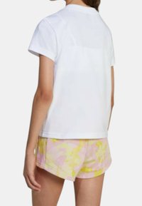 Camicia bianca a maniche corte con scollatura rotonda, abbinata a pantaloni corti rosa e gialli con un motivo a fantasia e un tessuto testurizzato.