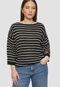 Haut surdimensionné à rayures noir et blanc avec un large décolleté et des manches trois quarts, associé à un jean taille haute bleu clair.