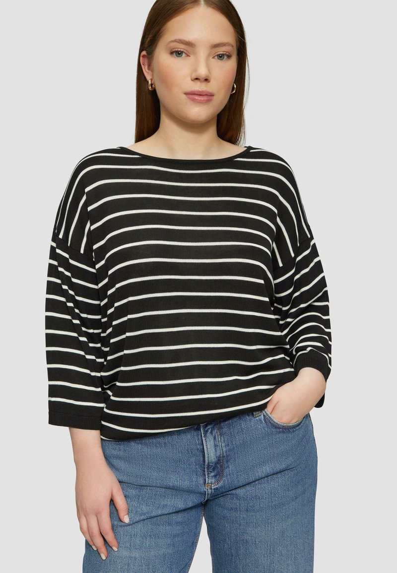 Haut surdimensionné à rayures noir et blanc avec un large décolleté et des manches trois quarts, associé à un jean taille haute bleu clair.