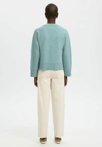 Light blue cropped sweater with ribbed hem and sleeves, worn over cream wide-leg pants. Soft texture, minimalistic design.