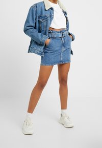 Denim takki, jossa on tekoturkiskaulus, yhdistettynä korkeavyötäröisiin farkkuhameeseen. Molemmat vaatteet ovat vaaleansinisiä, ja niissä on näkyvät ompeleet sekä taskut.