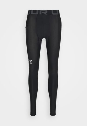 Mustat kompressiotrikoot, jotka on valmistettu sileästä ja joustavasta materiaalista. Niissä on leveä joustava vyötärö ja harmaalla värillä varustettu "UNDER ARMOUR" -logo sekä tyylitelty logo alhaalla jalan kohdalla.