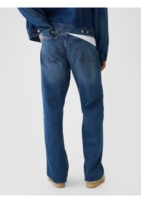 Jean en denim bleu vu de dos, avec une coupe droite, cinq poches et des zones délavées, avec des coutures visibles et des détails à la taille.