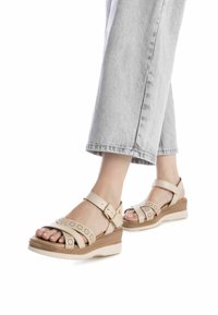 Sandali con zeppa beige con design a intaglio, cinturino alla caviglia regolabile e suola testurizzata. Abbinati a pantaloni in denim grigio chiaro.
