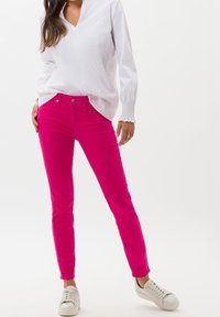 Fuchsiové slim-fit kalhoty s pěti kapsami, zkombinované s bílou košilí s dlouhým rukávem. Obuv tvoří světle zbarvené tenisky.