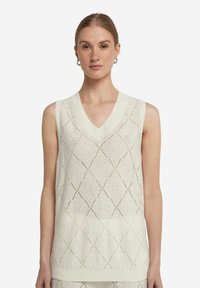 Stickad ärmlös topp i ljus elfenben med V-ringning, prydd med ett diamantmönster och ribbad nederkant. Tillverkad av andningsbart material.