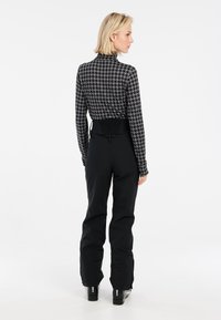 Schwarze Skihosen kombiniert mit einem figurbetonten, hochgeschlossenen Oberteil mit einem geometrischen Hahnentrittmuster in Schwarz und Weiß.