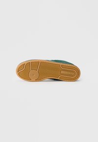 Tenis verde cu o talpă din cauciuc texturat, dotată cu un model pentru aderență și o talpă de gumă contrastantă. Design cu vârf plat și rotund.