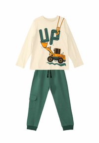 Grüne Baumwollhosen mit seitlichem Taschenpaar, kombiniert mit einem cremefarbenen Langarmshirt, das eine gelbe Baggergrafik und das Wort "UP" zeigt.